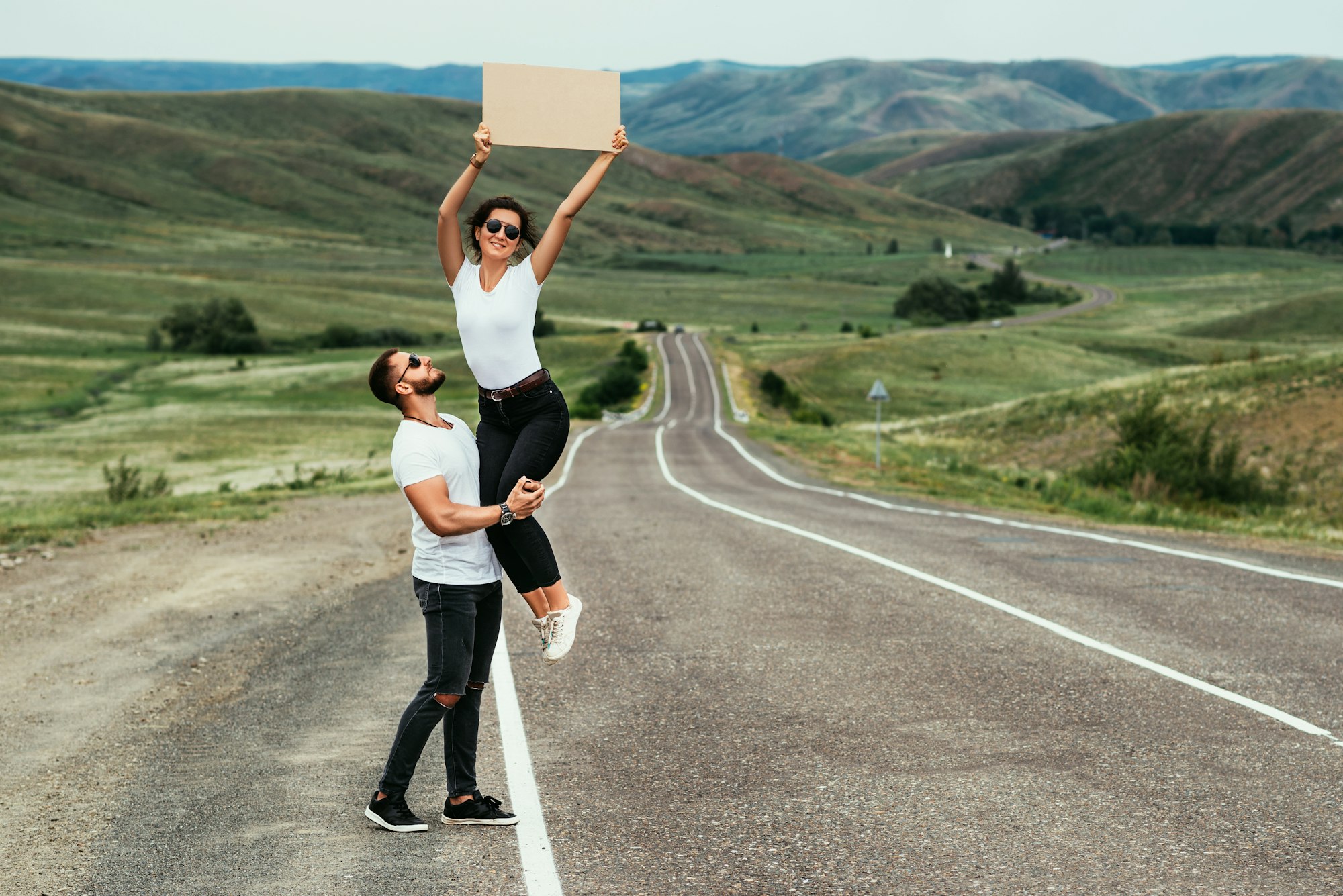 A young couple is voting on the road. A happy couple hitchhiking and voting with a sign on the road